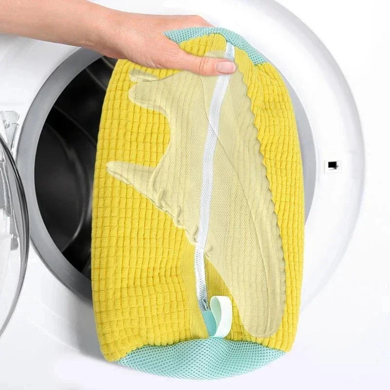 Hand placing a yellow mesh shoe laundry bag into a front-load washing machine