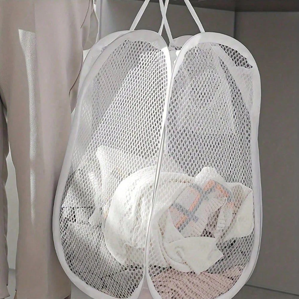 White pop-up mesh laundry hamper filled with clothes beside a bed